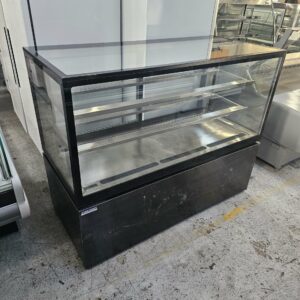 The ANVIL 1500MM DISPLAY FRIDGE, featuring metal shelves and a black base, sits on a concrete floor in a commercial space—perfect for anyone seeking quality restaurant equipment. MRCE