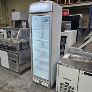 The BROMIC SINGLE DOOR DISPLAY FRIDGE, a tall white commercial display fridge with a glass door and empty shelves, is shown in a store or warehouse among other stainless steel appliances from Melbourne Catering Equipment. MRCE