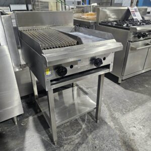 The LUUS 300 GRILL 300 CHARGRILL COMBO UNIT is a commercial stainless steel charbroiler with two control knobs, ribbed grilling surface, and open lower shelf, seen among other Melbourne Catering Equipment on a kitchen floor. MRCE