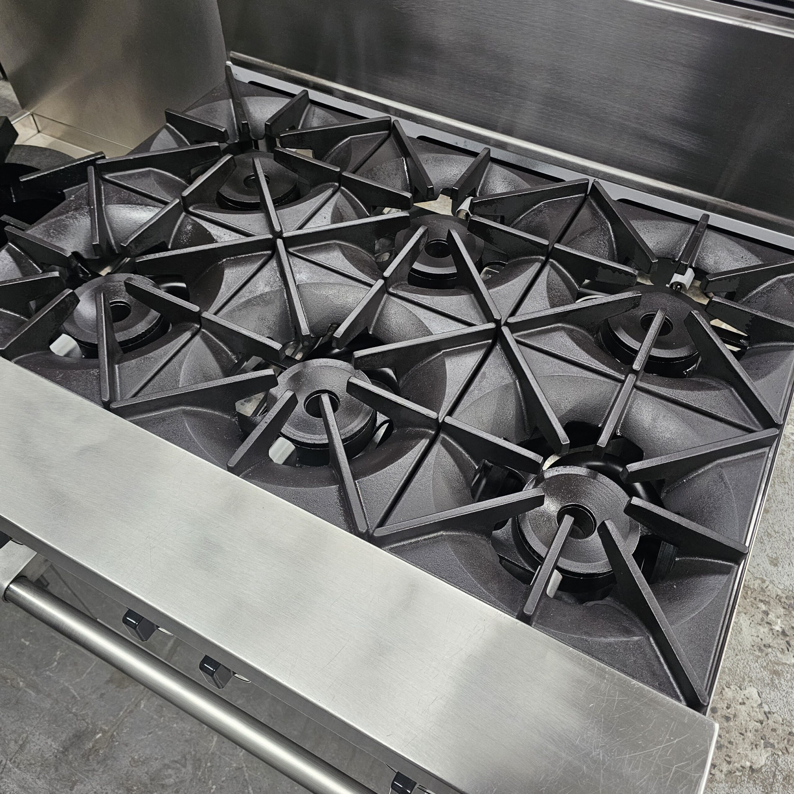 Six-burner commercial gas stove with black cast iron grates and a stainless steel finish, viewed from above in a kitchen setting. MRCE