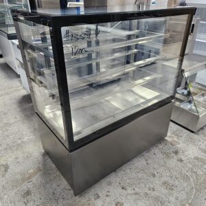 A stainless steel and glass display case with multiple shelves, situated in a commercial kitchen or store. The number #13556P and 120cm are written on the glass in white marker. MRCE