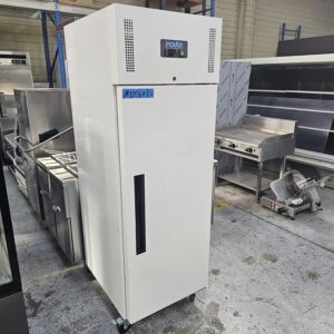 A tall, white commercial refrigerator with a digital display and air vents on top stands in a warehouse. It is surrounded by stainless steel kitchen equipment and has wheels for mobility. MRCE
