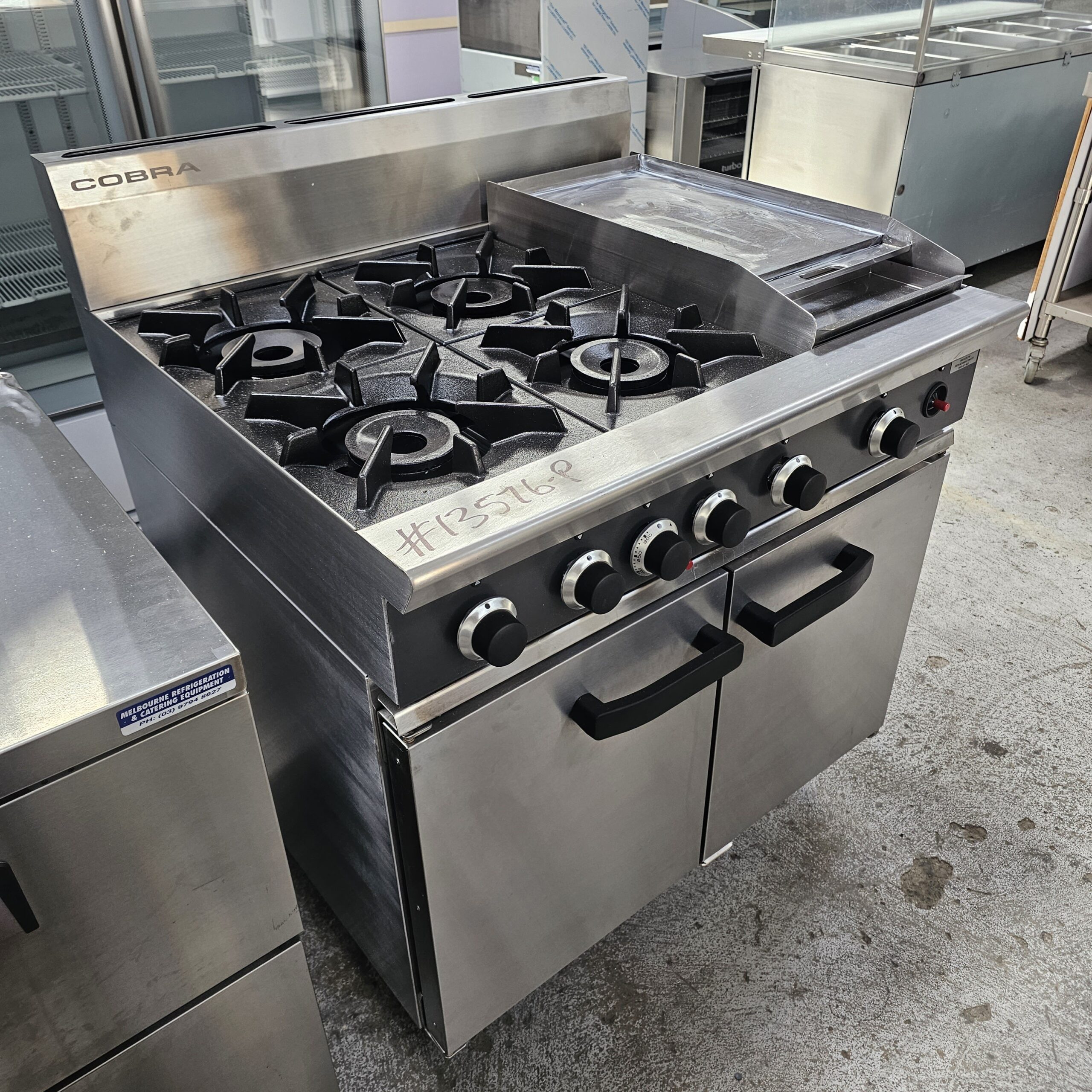A commercial stainless steel Cobra gas stove with four burners, a griddle, control knobs, and dual oven doors, situated in an industrial kitchen setting. MRCE