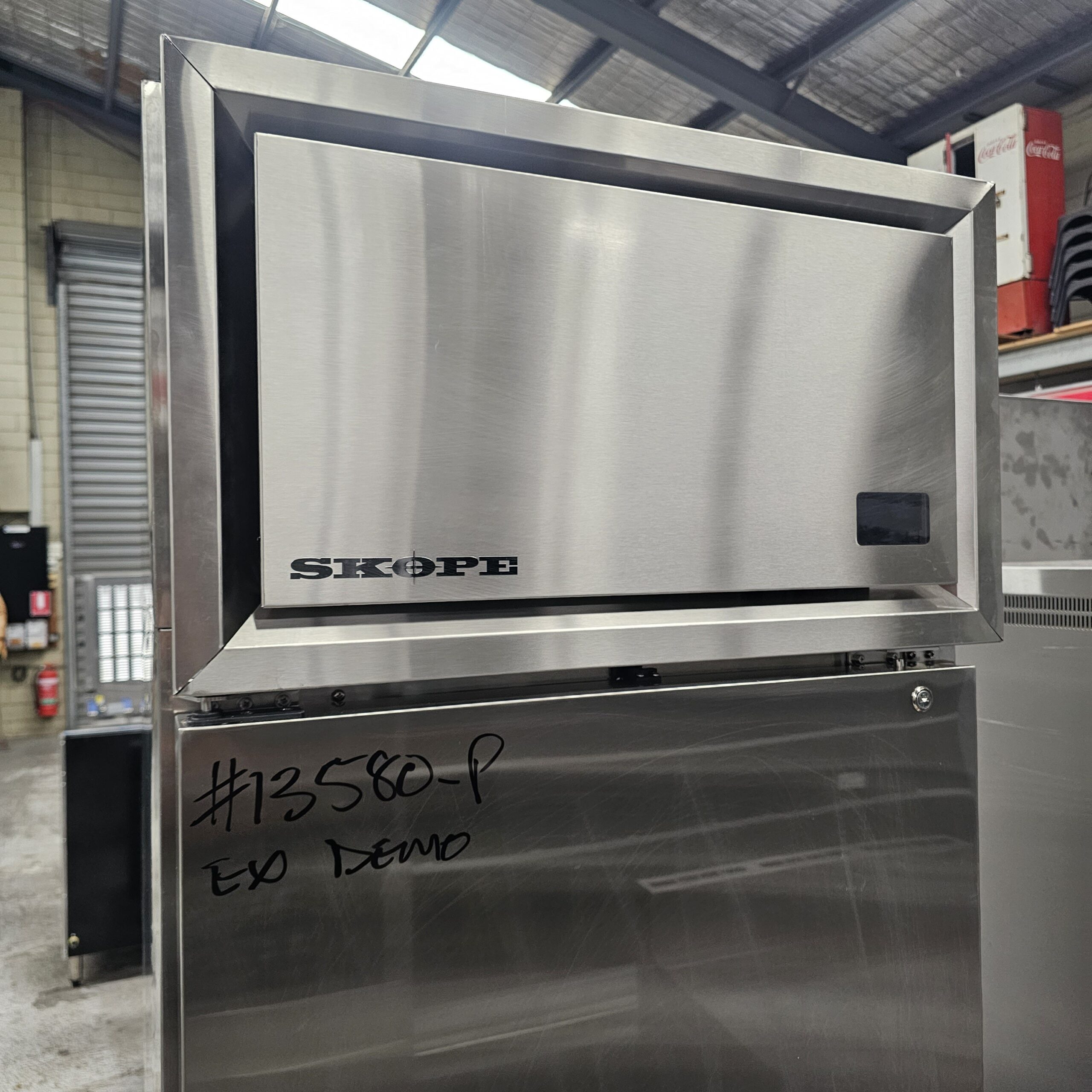 A stainless steel SKOPE commercial ice machine is shown in a warehouse setting, with #73580-P EX DEMO written in black marker on the front panel. MRCE