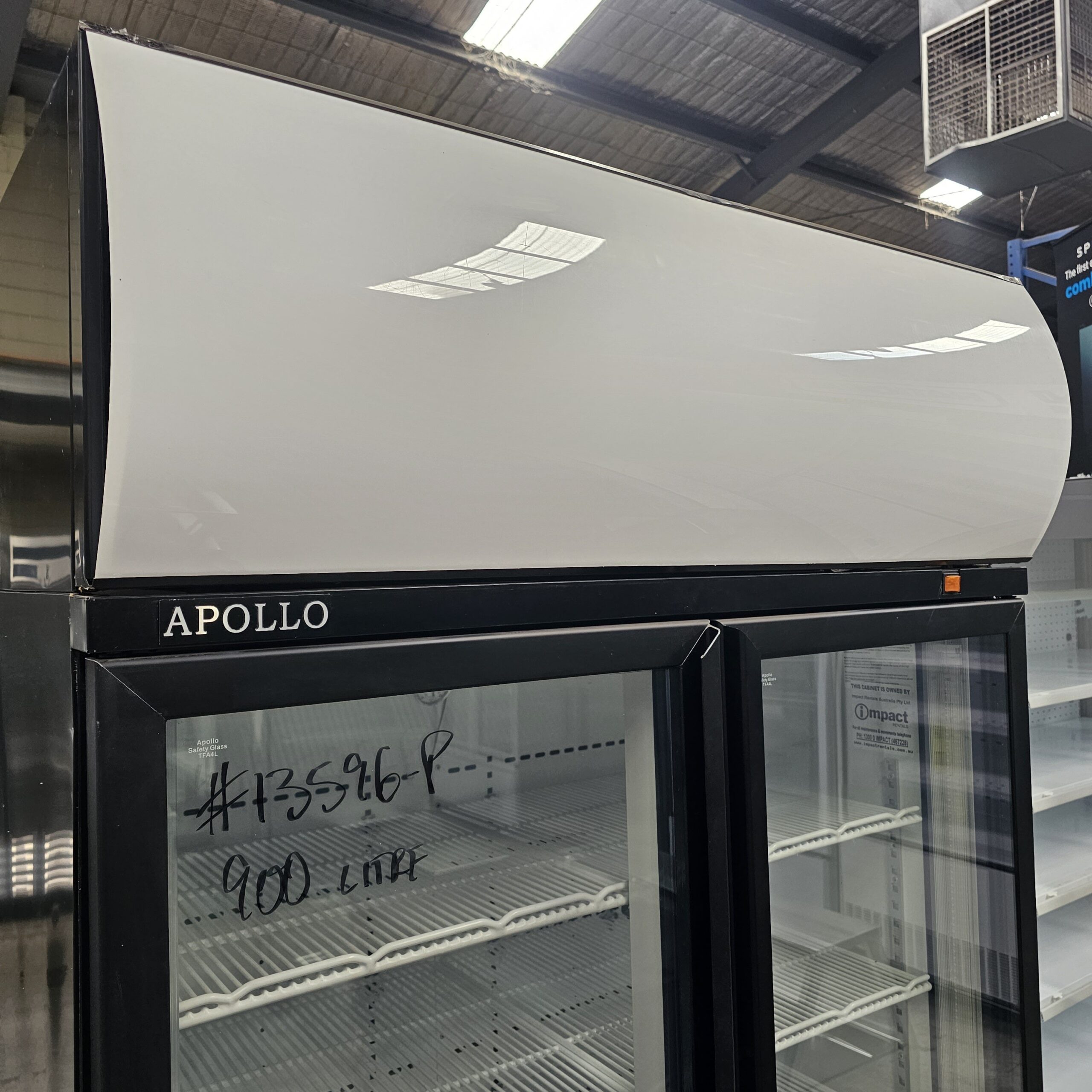 A commercial glass-door refrigerator labeled APOLLO with empty shelves inside, handwritten text on the glass reading #13596-P, 900 Ltr, and a white curved panel above the doors. MRCE