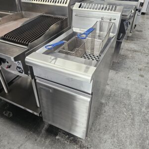 A stainless steel commercial deep fryer with two metal fryer baskets and blue handles, positioned next to a grill in an industrial kitchen setting. MRCE