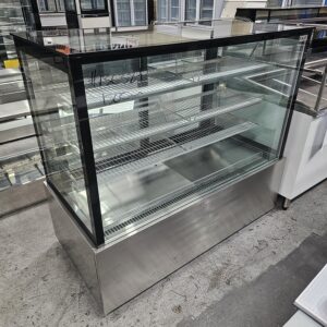 A large, empty commercial display refrigerator with glass sides and front, metal shelves, and a stainless steel base is shown in a store or warehouse setting. MRCE