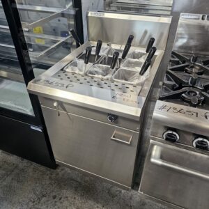 An EX DEMO NEW LUUS 9 BASKET PASTA COOKER with stainless steel finish stands beside a stove and a glass-front display case in a kitchen equipment showroom. MRCE