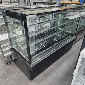 A large, black-framed glass display case with multiple shelves is shown on a warehouse floor. The case is empty, and there is a price written on the glass in white marker. MRCE