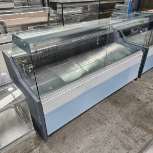 A large, empty refrigerated display case with glass panels and metal shelves, standing on a concrete floor in what appears to be a commercial or industrial setting. MRCE